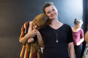 Christine Plastow and Sinead Costelloe in rehearsal. Two young women laugh and hold each other